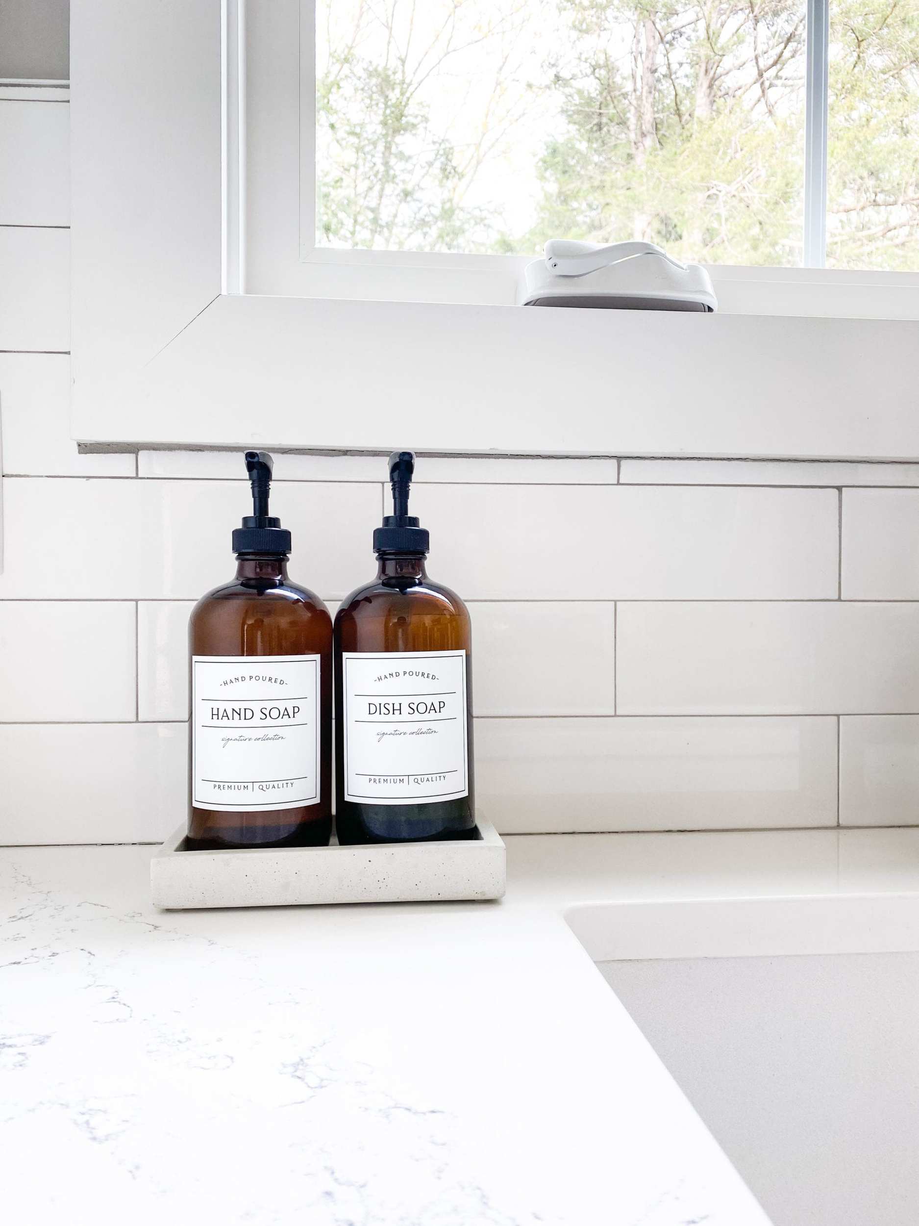 Amber hand and dish soap bottles with black pumps in a soap tray with a white subway tile backsplash