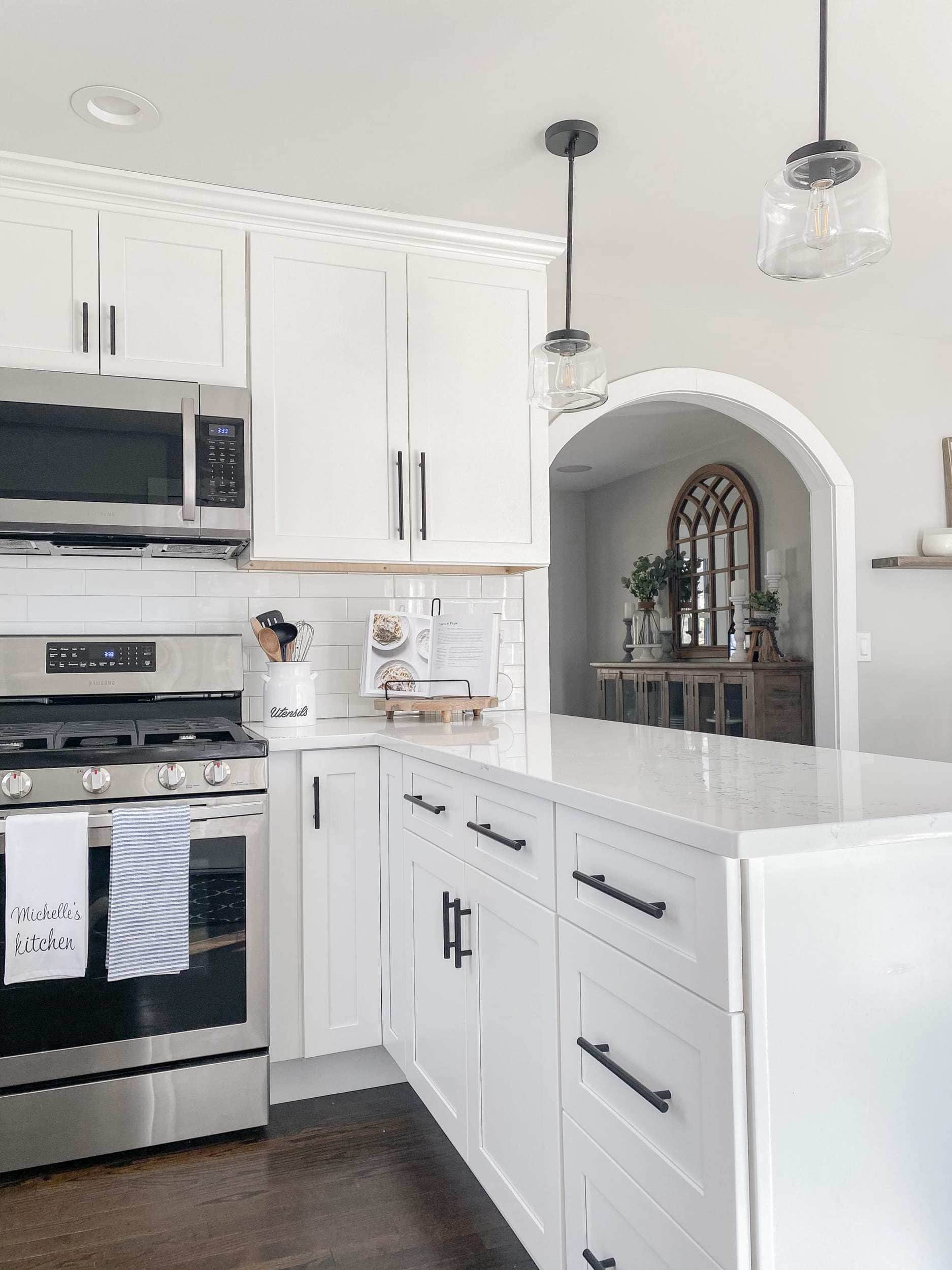 the after of the kitchen renovation with white shaker style cabinets, black modern farmhouse pulls, black simple schoolhouse pendants, and samsung appliances 