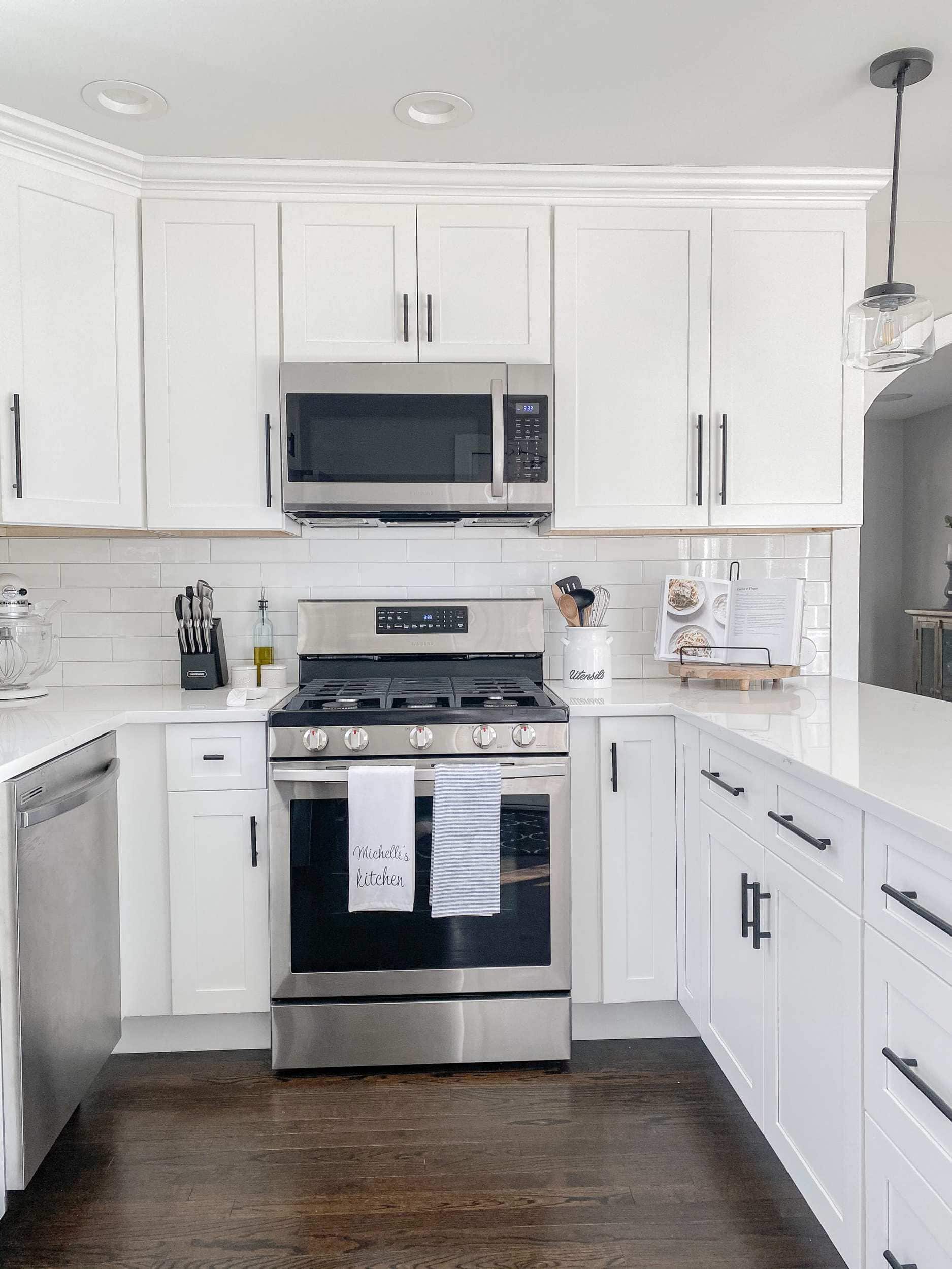 the after of the kitchen renovation with white shaker style cabinets, black modern farmhouse pulls, black simple schoolhouse pendants, and samsung appliances 