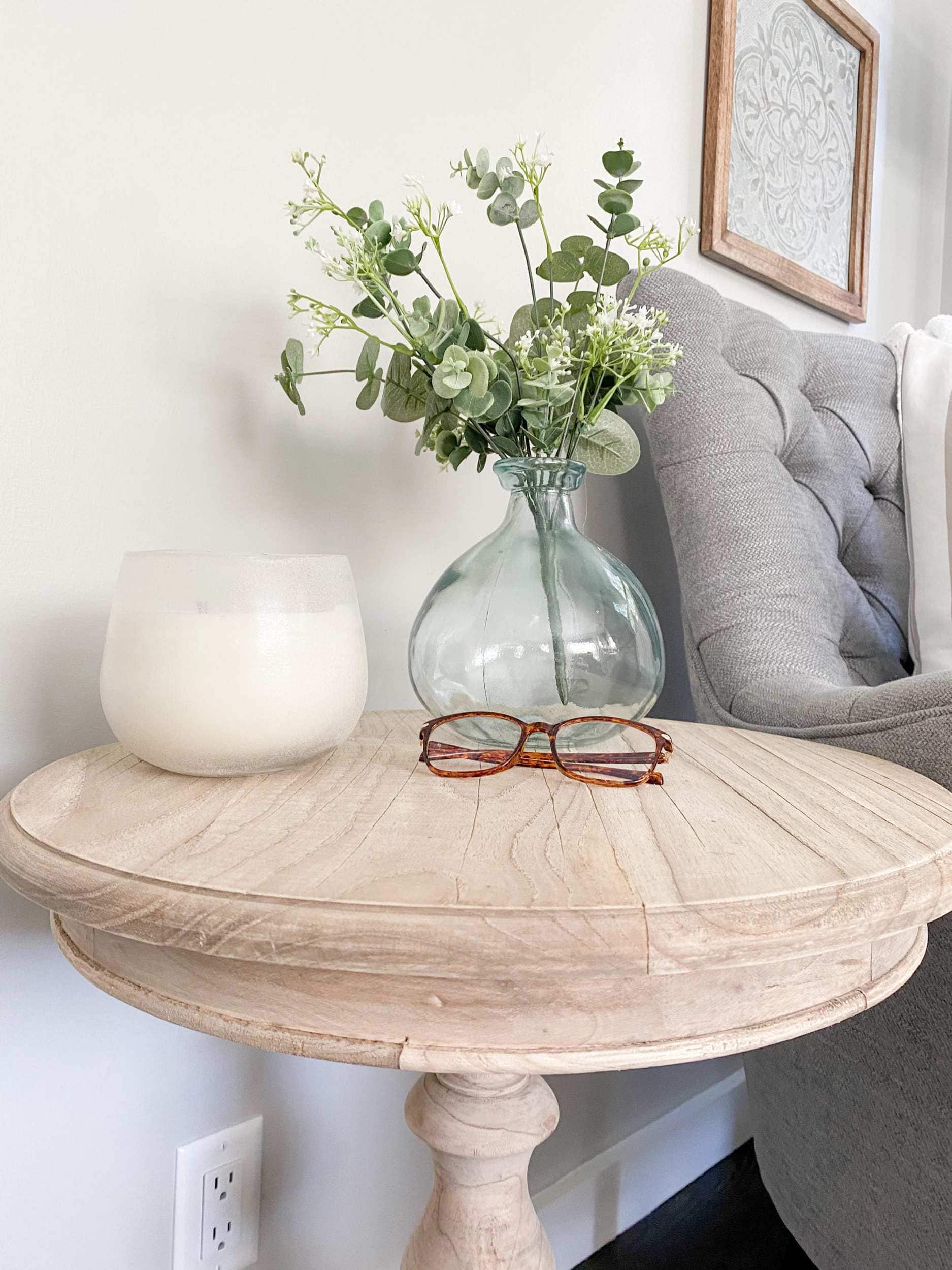 unfinished wood table with candle, reading glasses, and demijohn