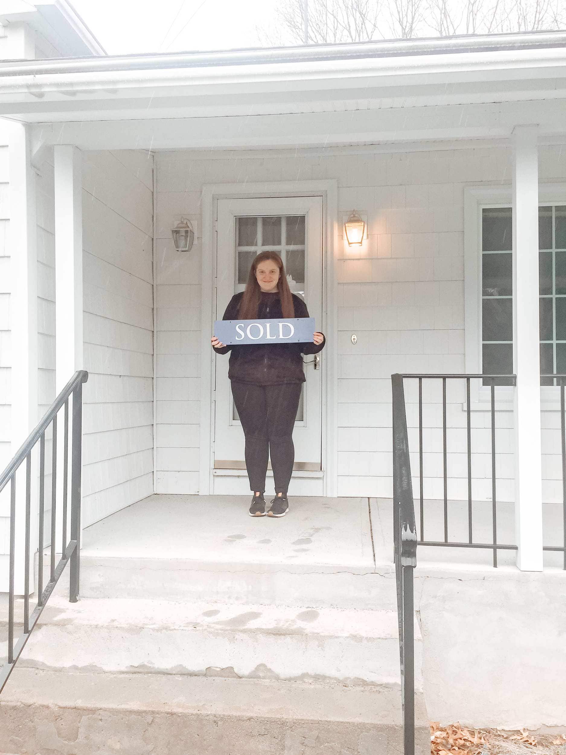 Michelle Frohman, author of the acorn hill home holding her sold sign on the front porch. 
