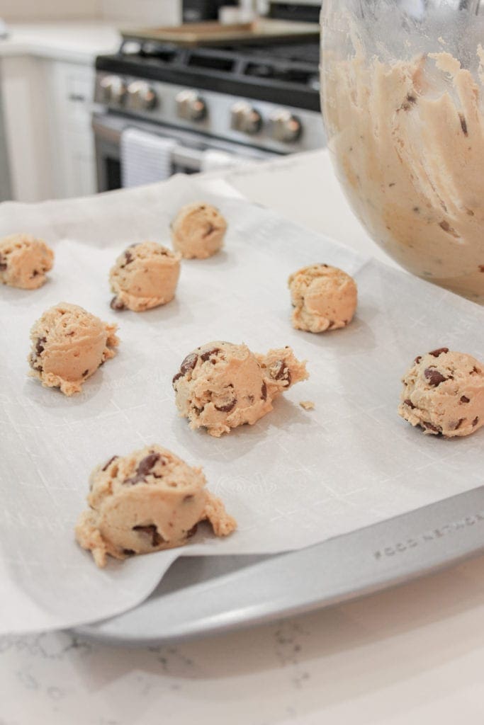 Heaping tablespoons of cookie dough on a parchment lined cookie sheet ready to go in the oven. 