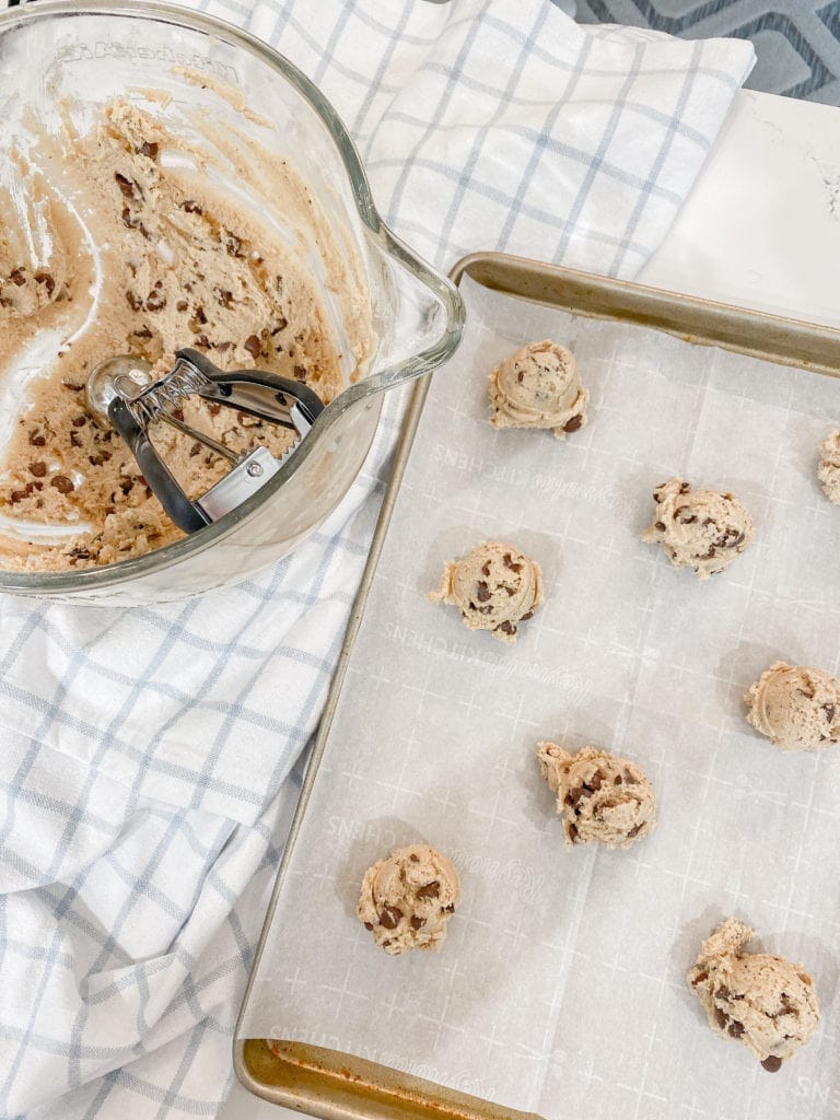 Tablespoons of cookie dough on a parchment lined cookie sheet with the mixing bowl of dough.