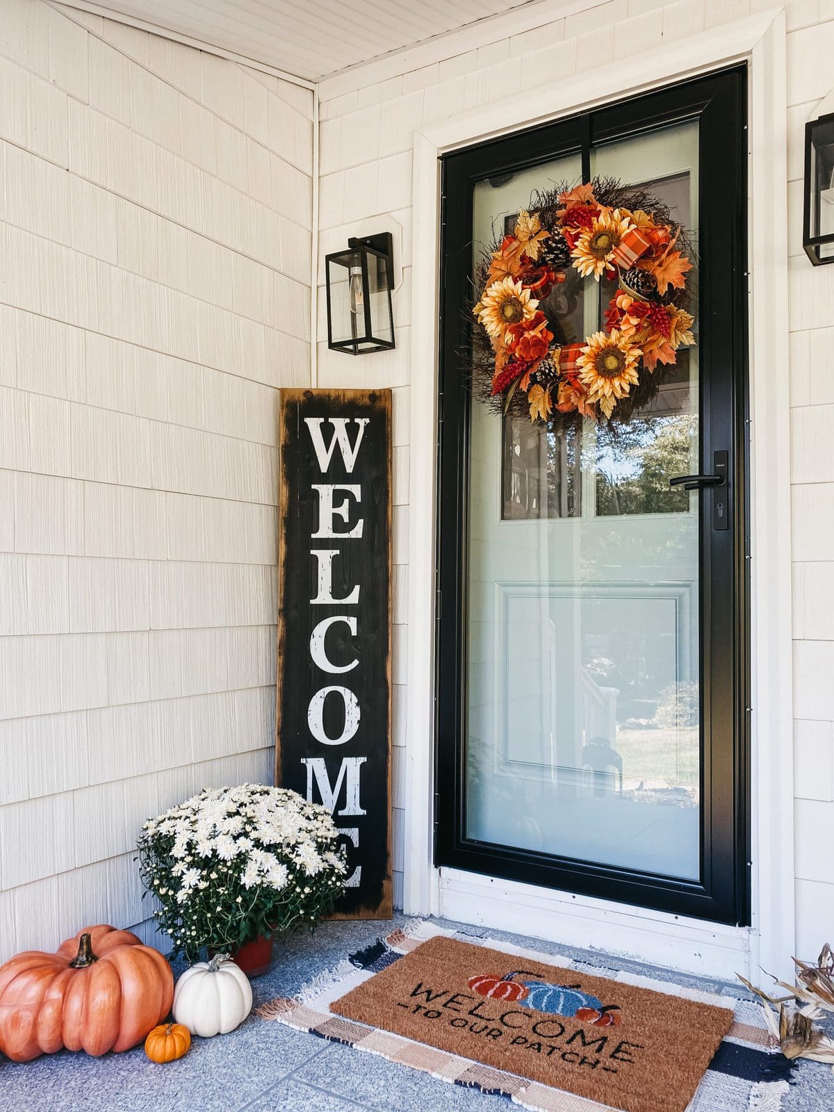 welcome sign fall front porch with white mums, real and faux orange pumpkins, black storm door, welcome mat, and benjamin moore wythe blue front door 