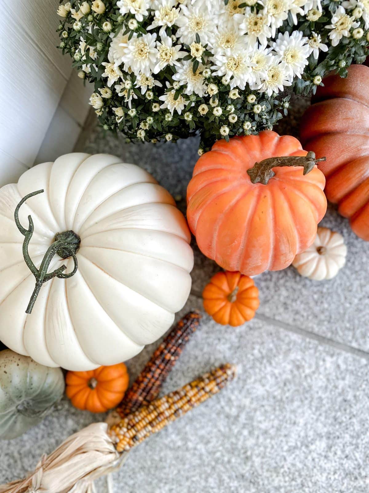 Faux cream pumpkin, faux orange pumpkin, real mini pumpkins, white mums, and colored corn for fall front porch decor