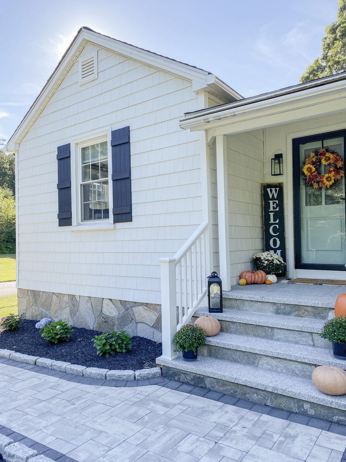 White cottage with black shutters and faux rock facade on foundation fall decor front porch