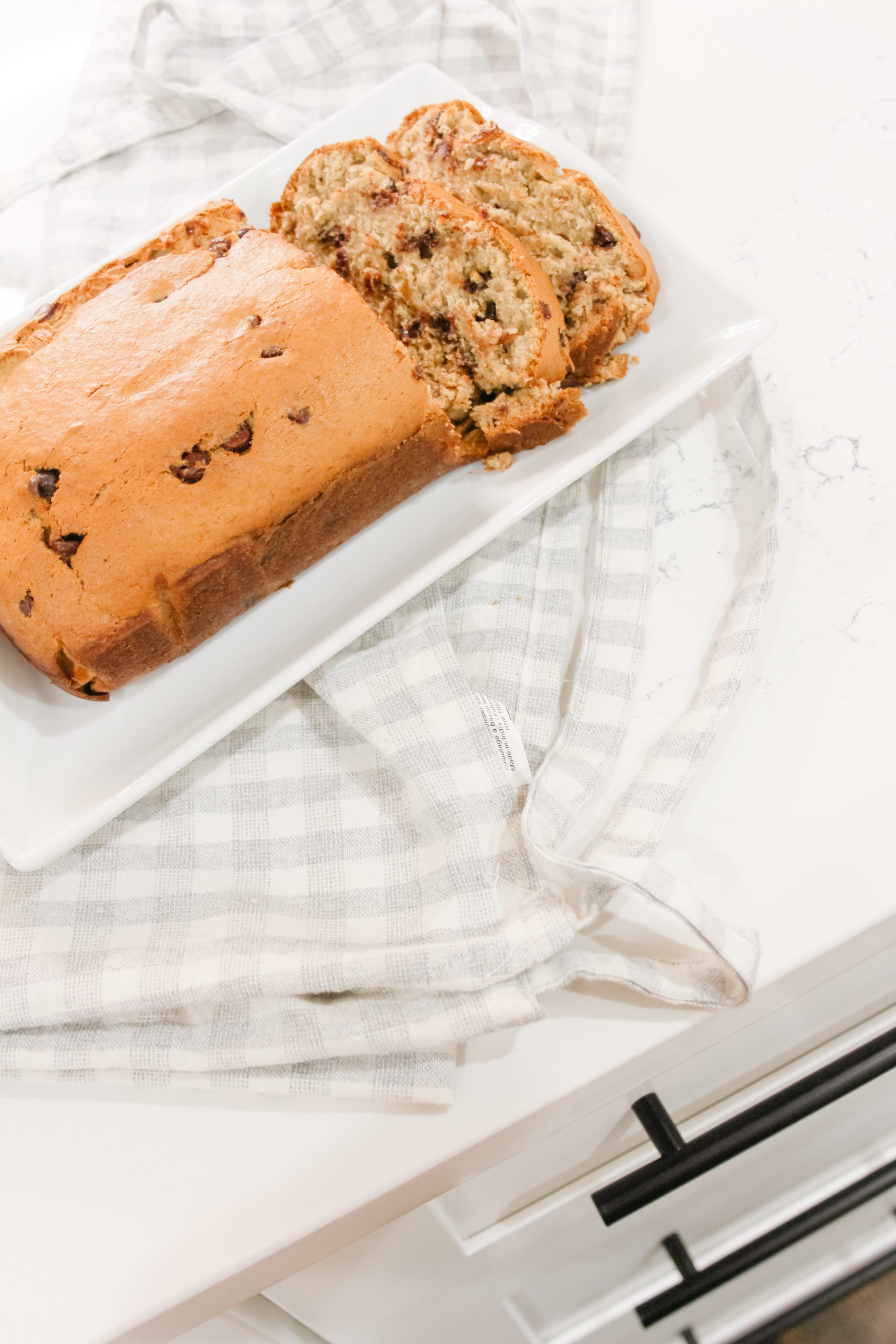 Easy moist chocolate chip banana bread on a white serving dish with a blue and white plaid apron. 