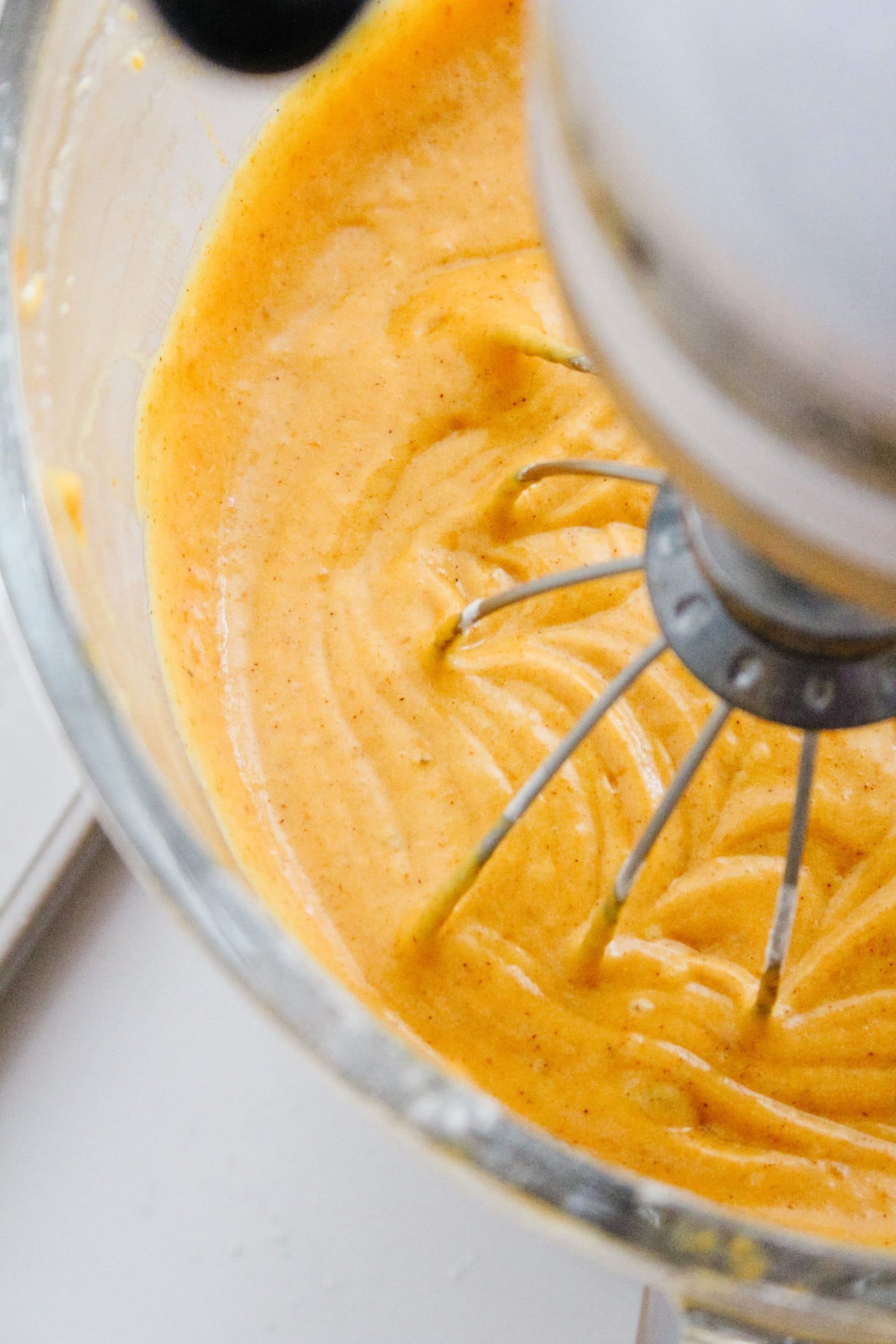 Pumpkin sheet cake batter in a kitchenaid mixer with a whisk attachment and a clear mixing bowl