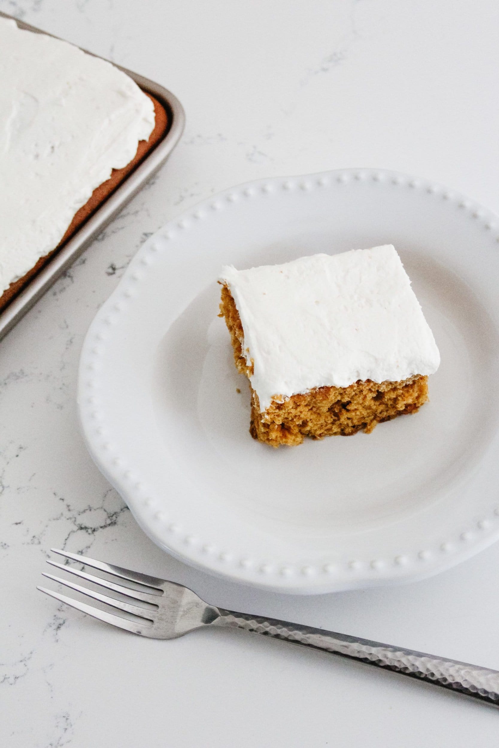 Pumpkin sheet pan cake in a sheet pan with whipped cream cheese frosting on a white quartz countertop