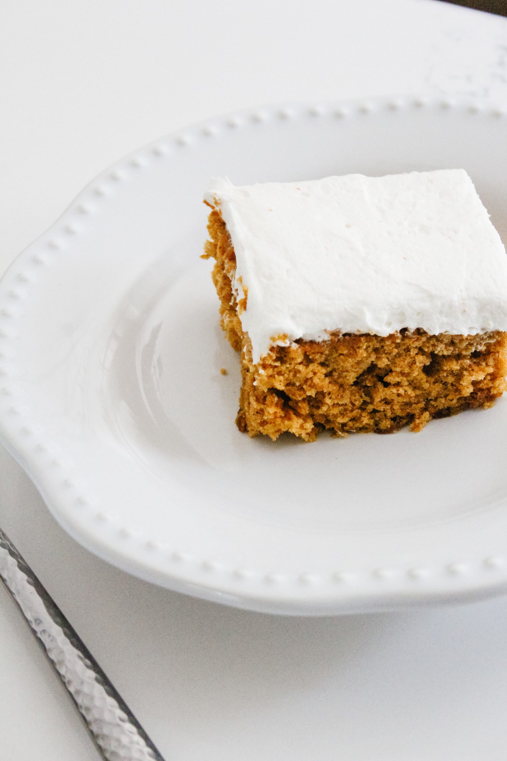 Pumpkin sheet pan cake with whipped cream cheese frosting on a white quartz countertop on a pottery barn plate