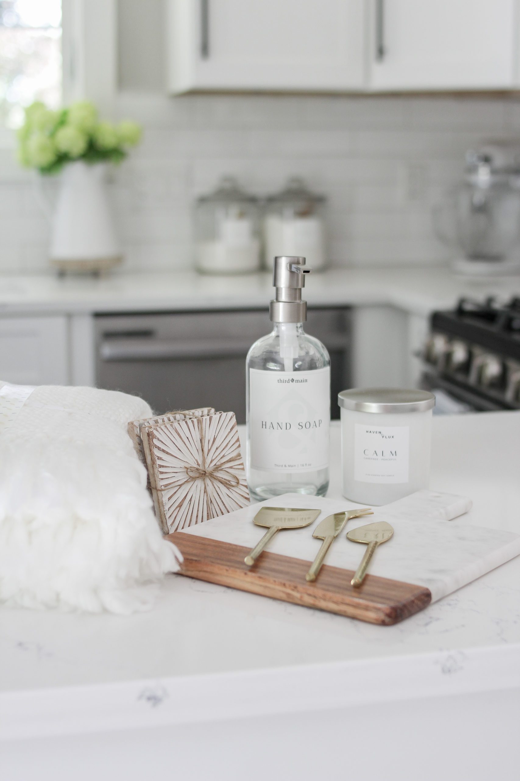 for the decor lover home decor box from third and main featuring a third & main hand soap bottle, haven + flux calm luxury candle, mango wood starburst coaster, cream knit tasseled throw, mango wood acacia and marble wood cutting board, golden cheese knife set