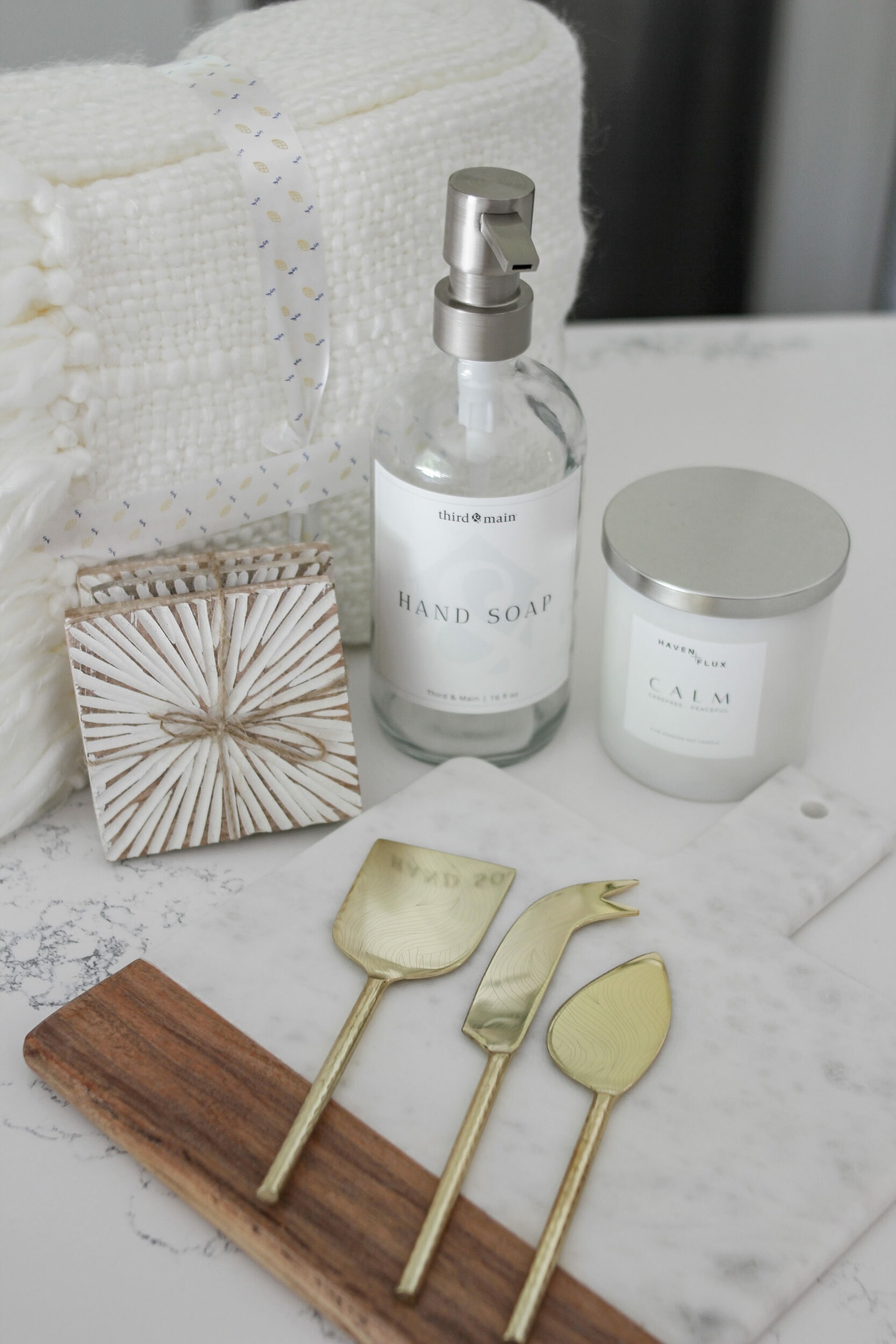 for the decor lover home decor box from third and main featuring a third & main hand soap bottle, haven + flux calm luxury candle, mango wood starburst coaster, cream knit tasseled throw, mango wood acacia and marble wood cutting board, golden cheese knife set