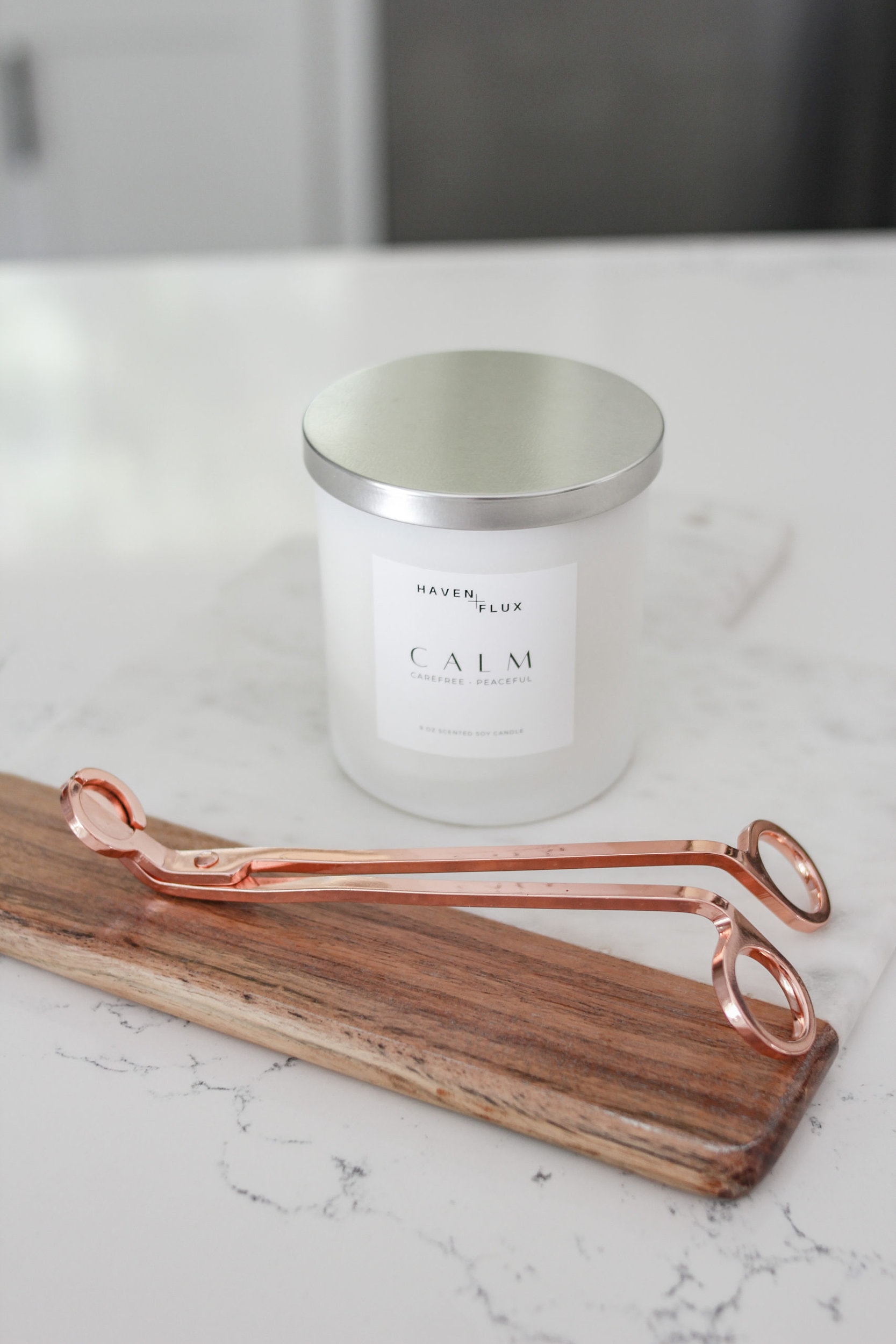 Third & Main Haven + Flux calm luxury candle on a mango wood acacia and marble cutting board with rose gold candle trimmers