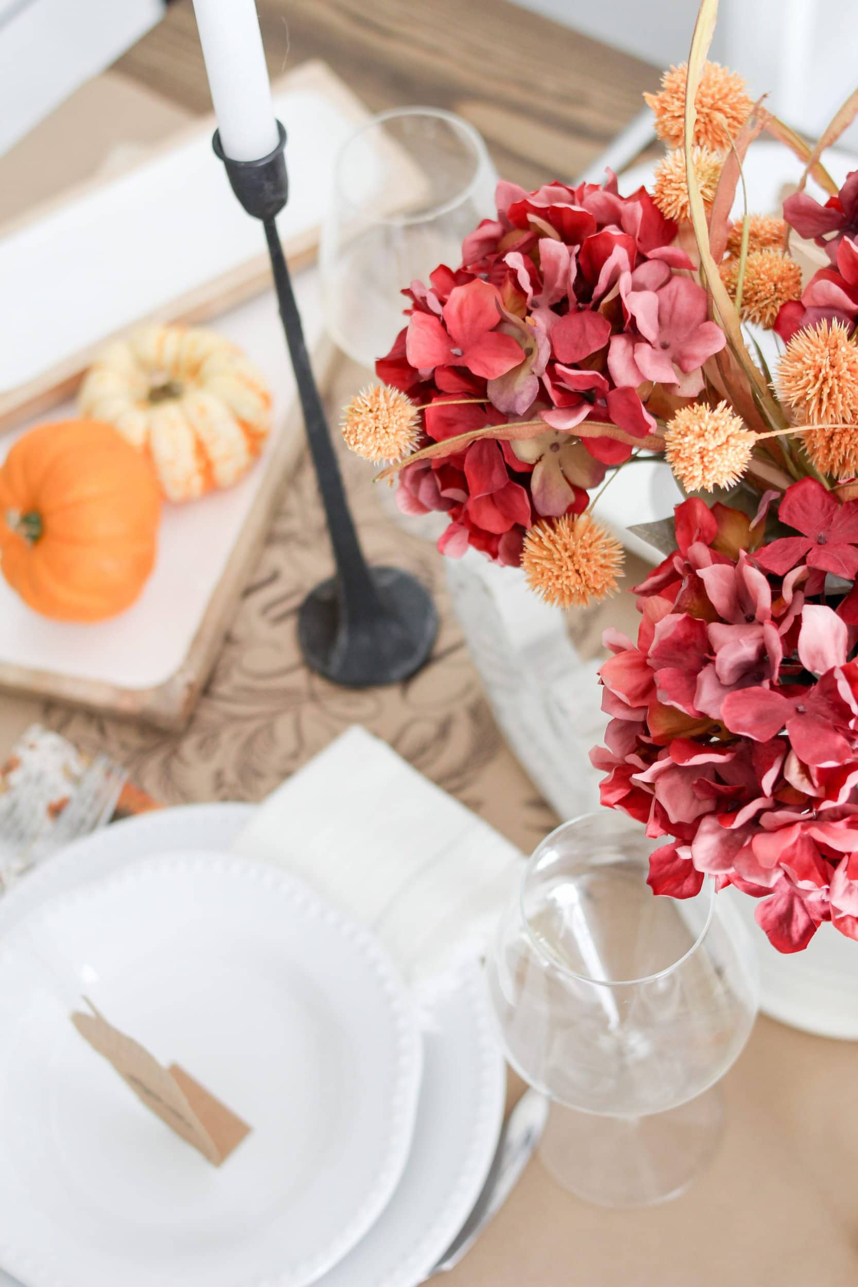 Fall Thanksgiving tablescape table decor with red hydrangeas, orange fall stems, jack-be-little pumpins, gourds, wind elgasses, black cast iron candlesticks, and white plates
