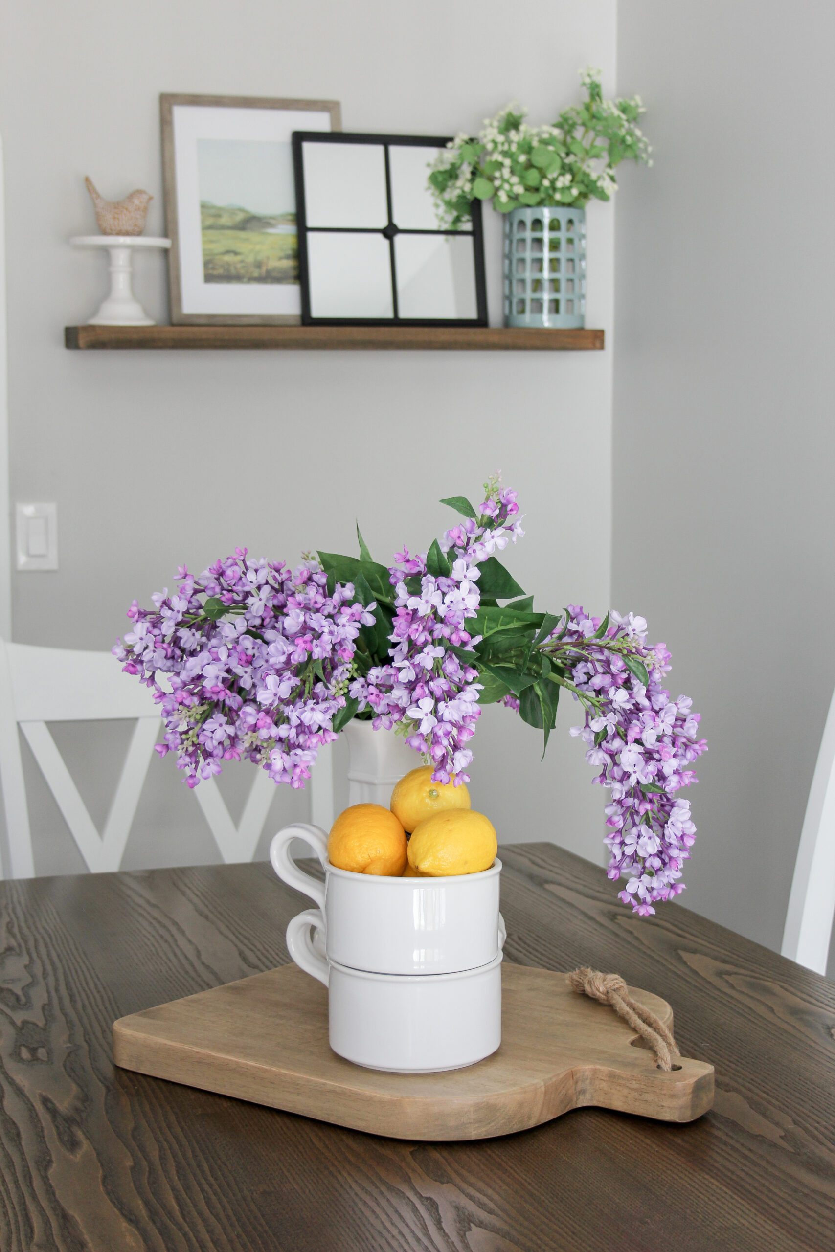 faux lilacs with lemons on a cutting board with an ironstone pitcher with a modern farmhouse floating shelf in the background
