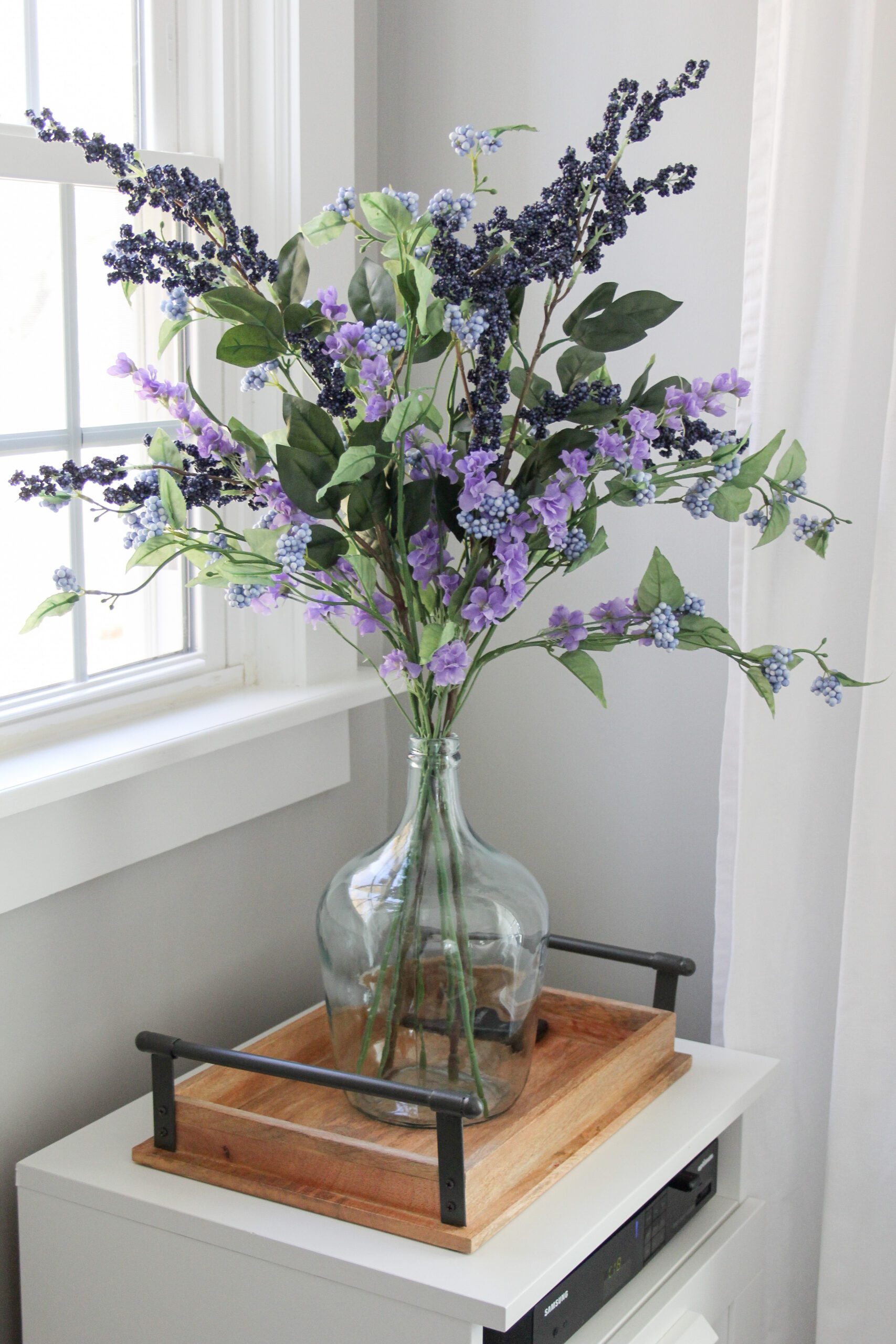 blueberry stems with purple delphinium in a glass demijohn