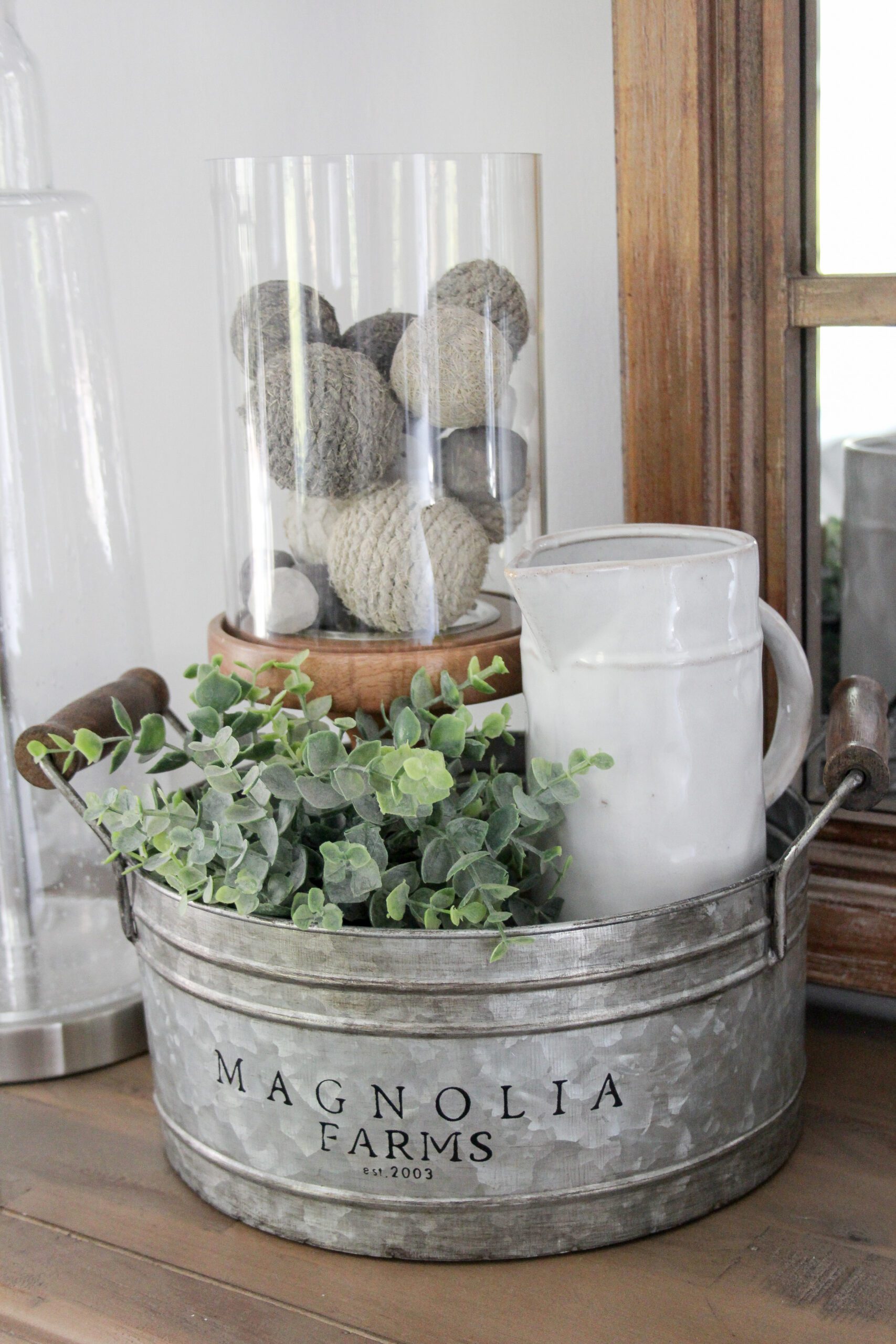 magnolia home galvanized bucket with a eucalyptus plant, thin ceramic pitcher, wood hurricane with organic filler