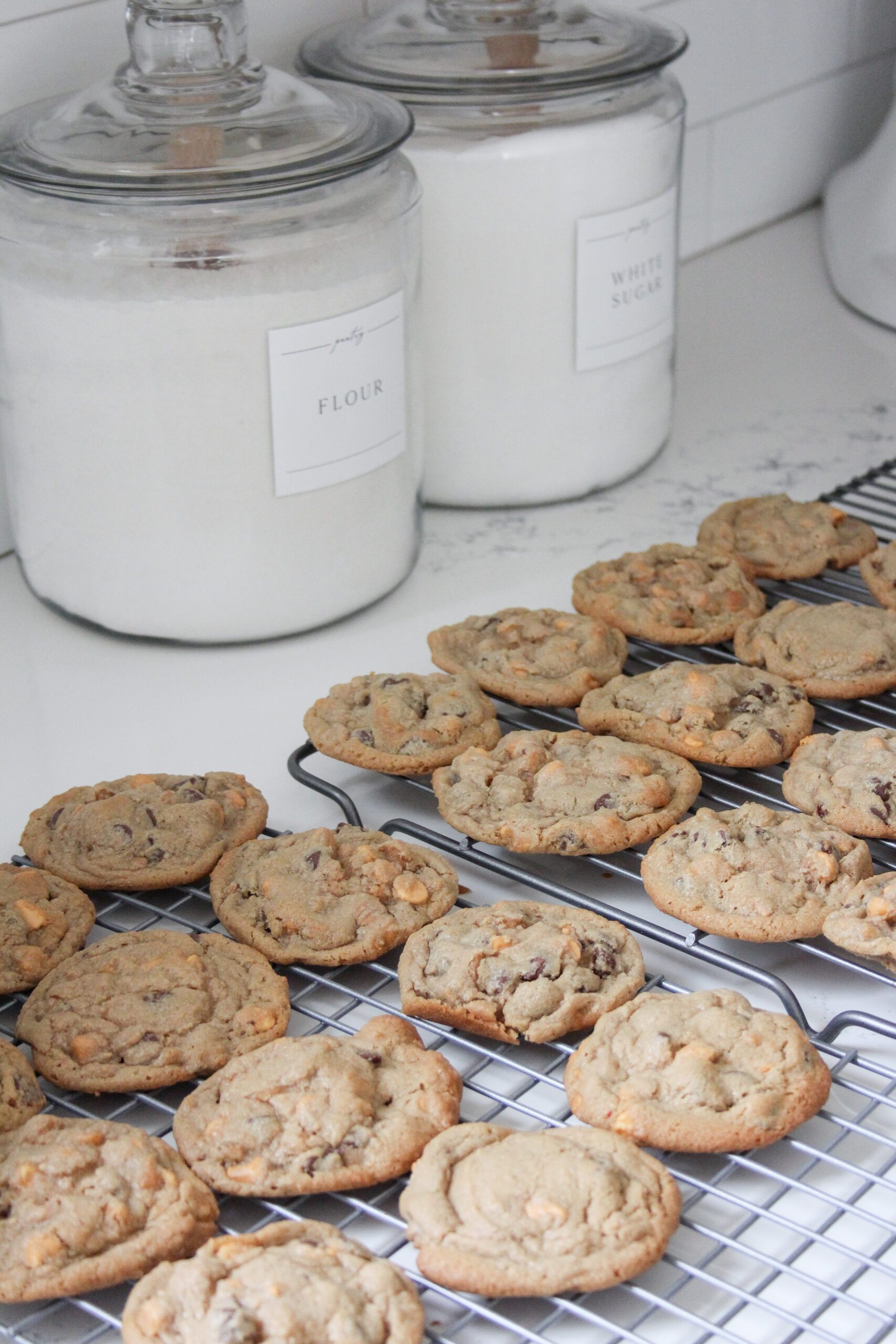 peanut butter chocolate chip butterscotch cookies on a cooling rack on a white quartz countertop with glass jars of flour and sugar. 