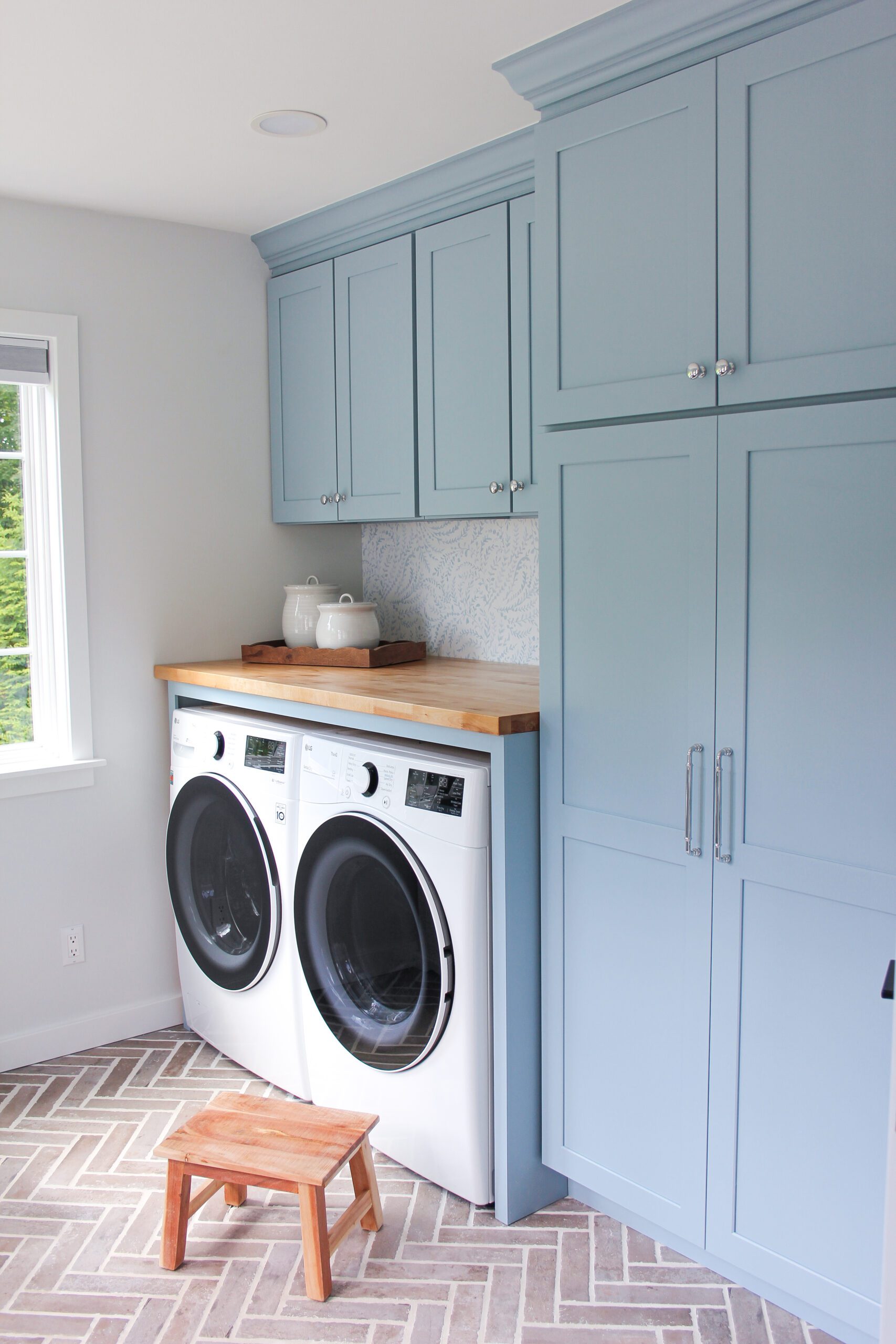 cottage laundry room with dockside by sherwin williams blue cabinets, serena and lily backsplash wallpaper, butcher block countertop, and tob knobs hardware